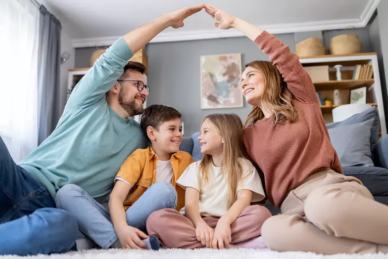 An affectionate family scene showing a mother, father, and kids forming a symbolic house shape with their hands, illustrating a cozy and loving home life.