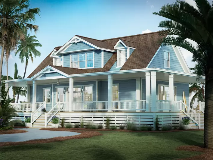 The front exterior of a large beach house with blue siding, large white windows and accents, and a long front porch surrounded by landscaped grass and palm trees.