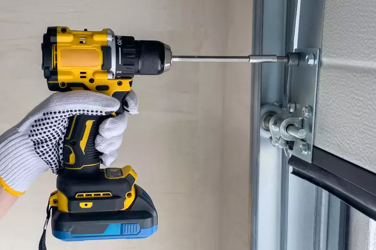 Person with an electric drill adjusting a section of a garage door.