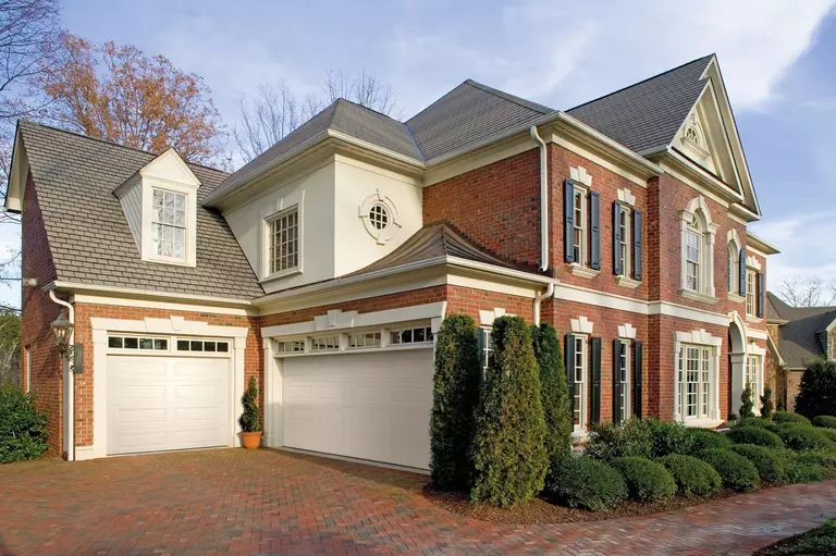 White double and single Amarr Lincoln garage doors with clear windows connected to a brick house.