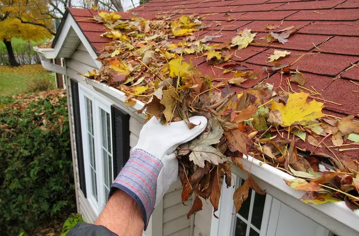 Gloved hand cleaning leaves from off the roof of a home