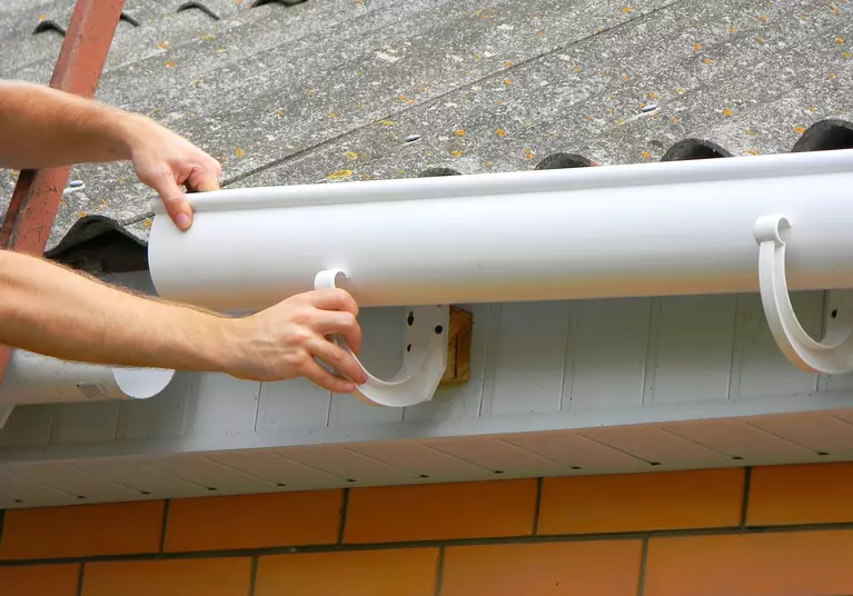 Hands adjusting the installation angle of gutters on a house.