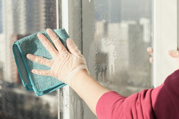 A person wiping down the glass of a patio door with a cloth.
