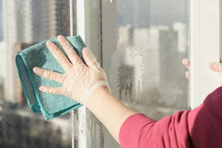A person wiping down the glass of a patio door with a cloth.