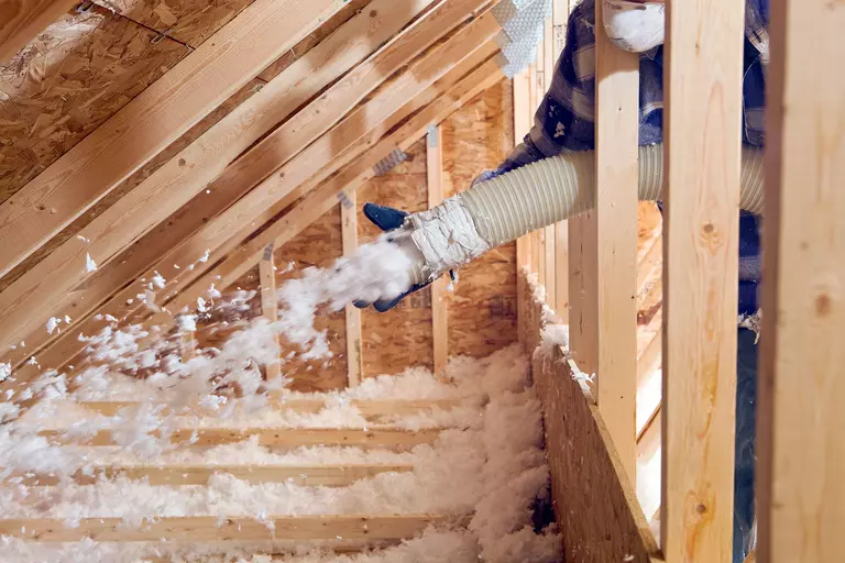A professional applying blown-in insulation within a home’s attic.