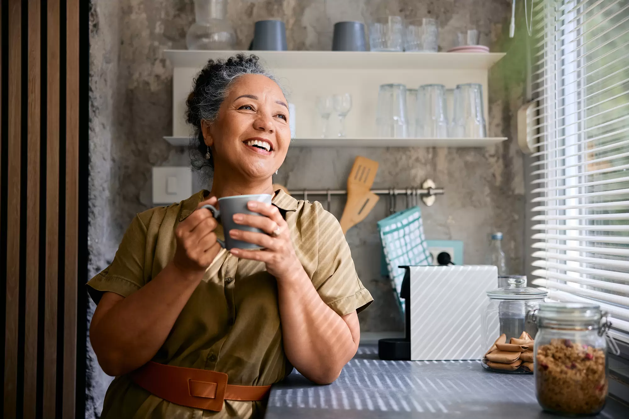 Woman drinking coffee next to a large window letting in sunlight.
