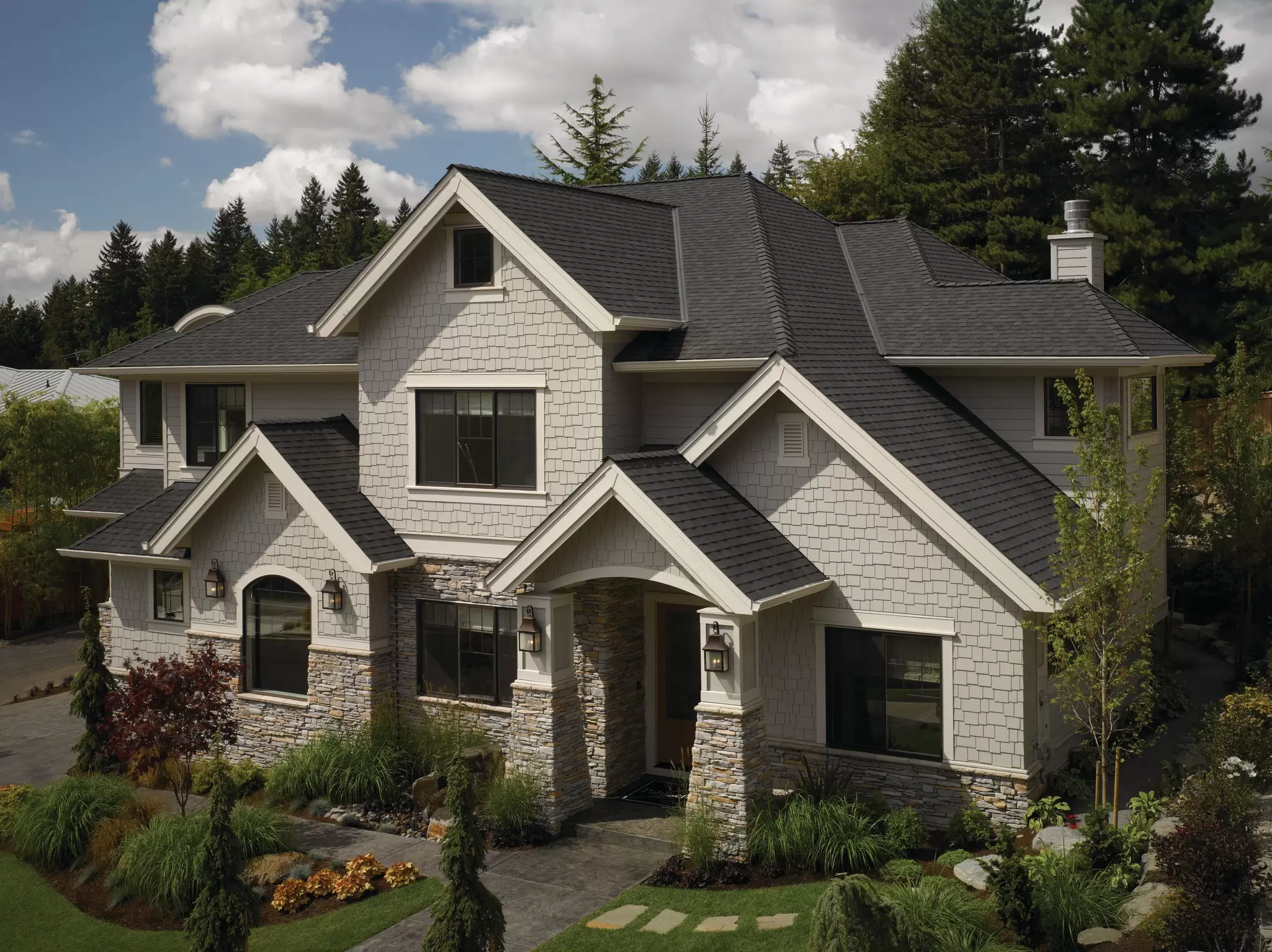 Two-story craftsman-style home with gray shake siding, stone accents, and black-framed windows.