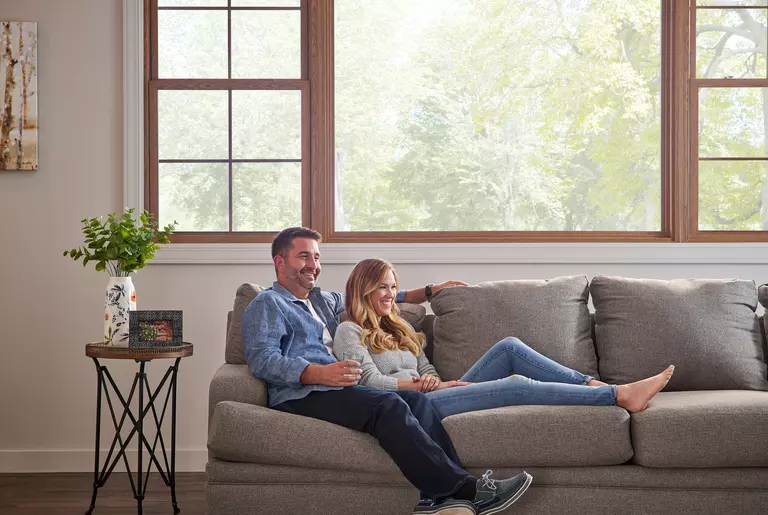 Man and woman on a sofa in front of a set of wood-clad picture and double-hung windows.