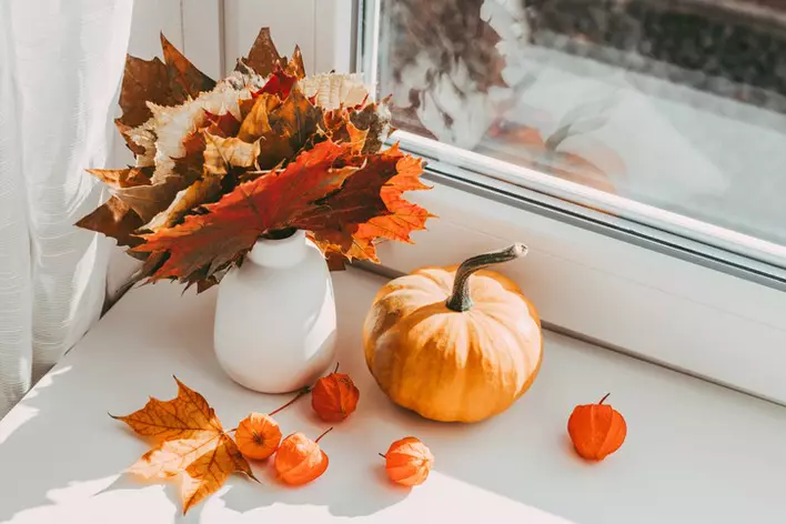 Seasonal autumn home decorations with decorative pumpkins and fall leaves on a windowsill