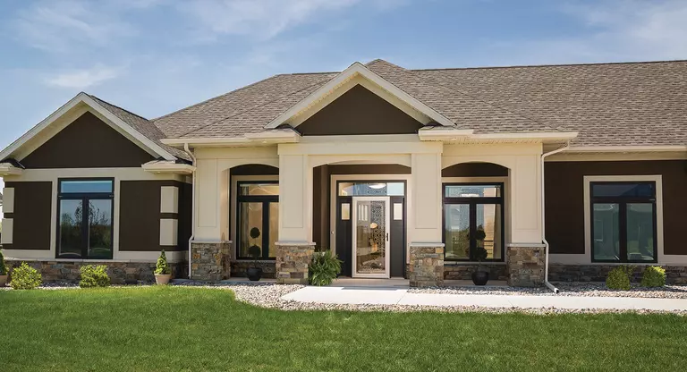 Exterior of a home with four similar black windows and a front door with sidelites, transom, and a storm door.