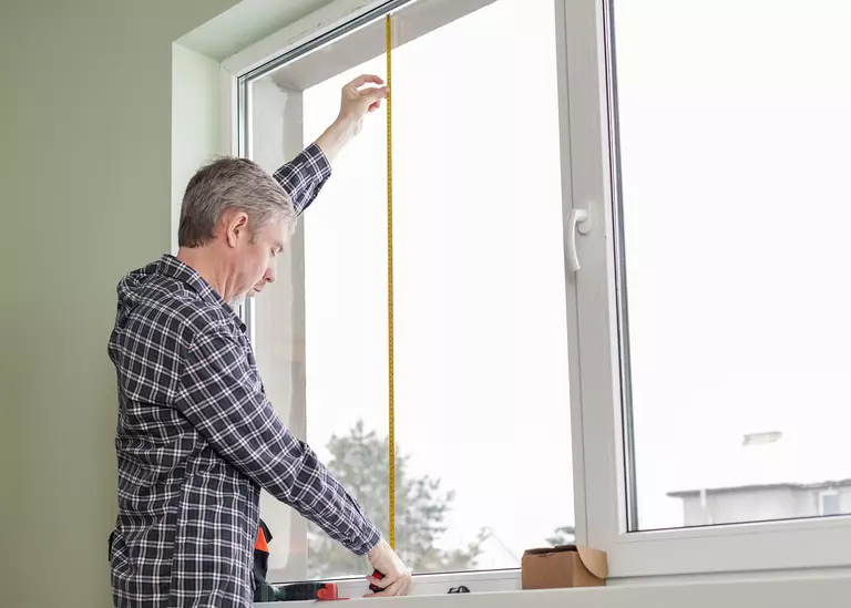 Man using a tape measure to check the height of a window.