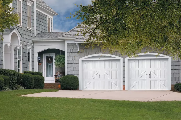 Dual white wooden garage doors on a Cape Cod-style home.