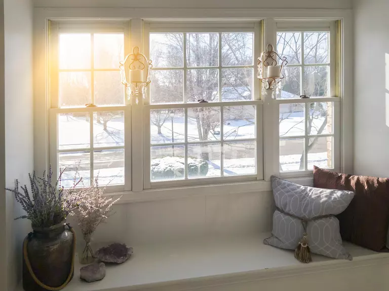 Large paned windows over a window seat overlooking a large piece of land outside
covered in snow.