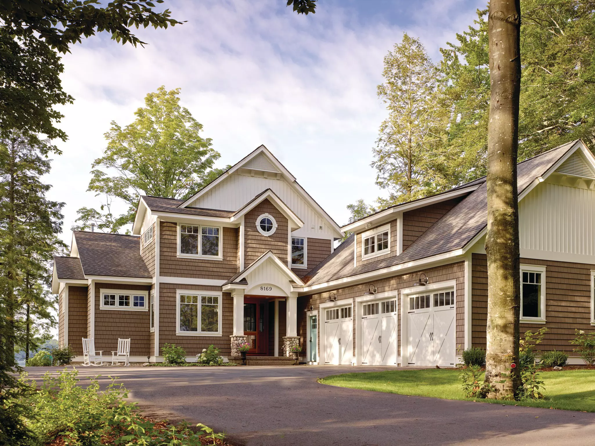 White and brown home with mastic siding, three garage doors, and driveway shown.