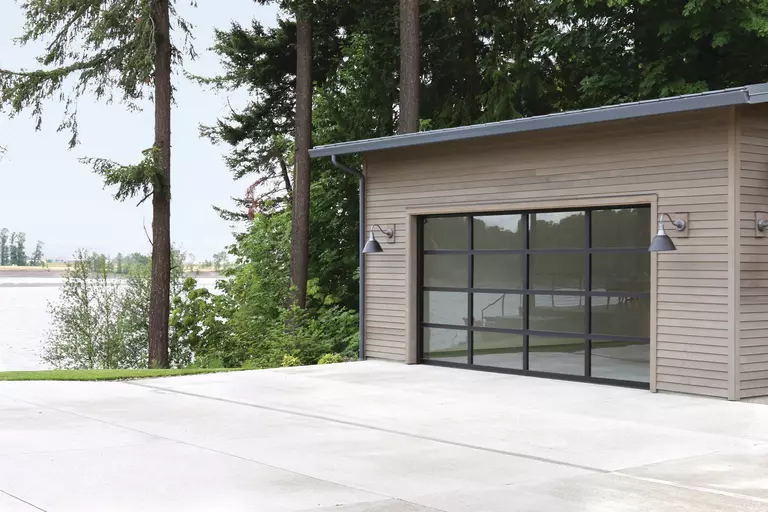 Aluminum-framed garage door with large glass panels near a body of water.