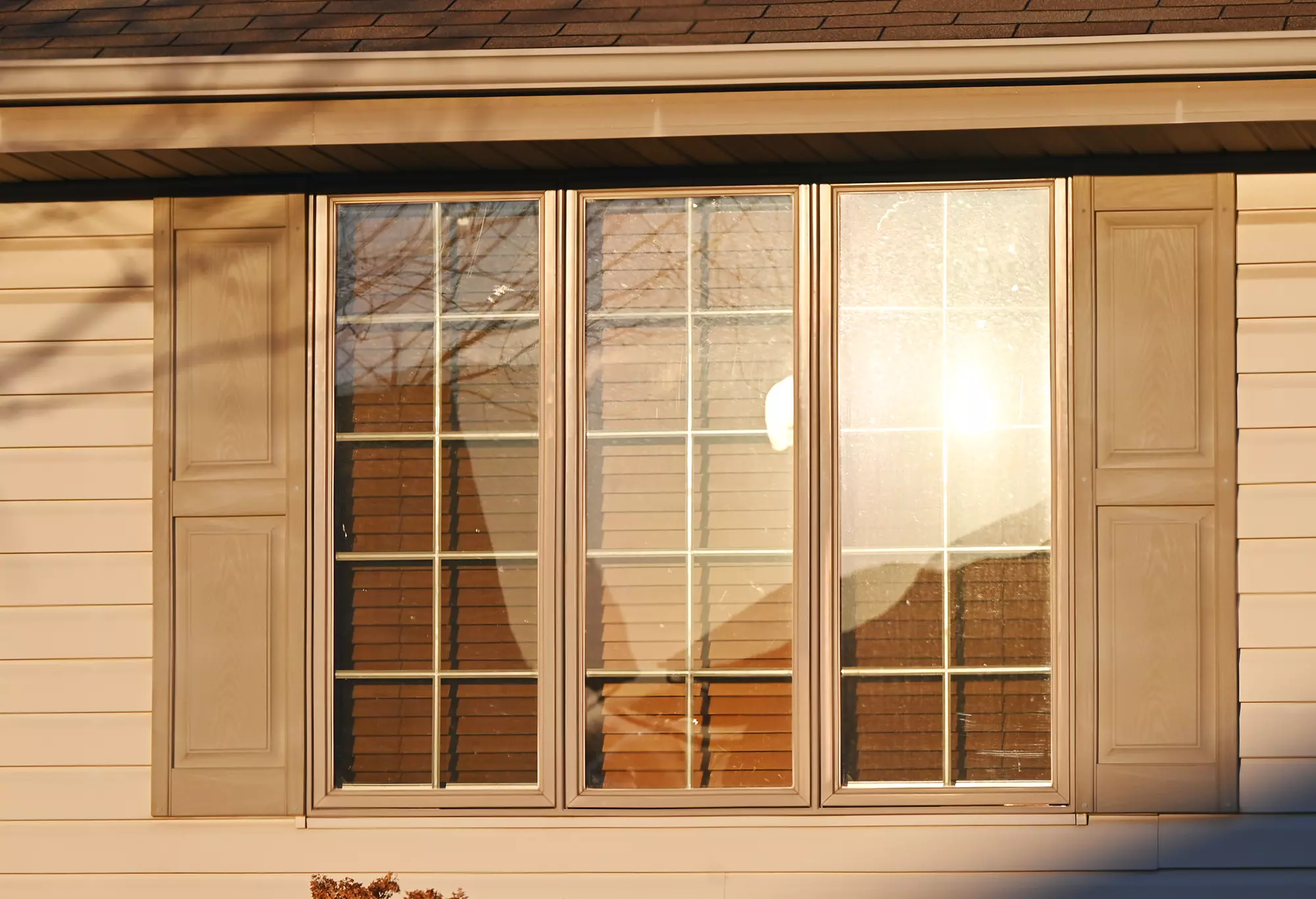 Exterior view of sunlight shining on windows with shutters and blinds.