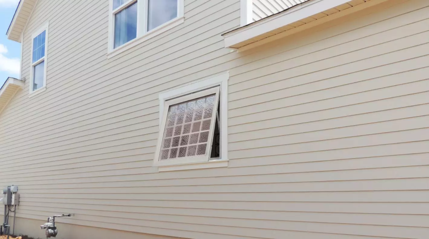 Awning window open on the side exterior of a vinyl-sided home.