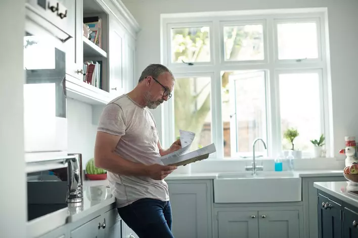 Man reading papers in a grey-toned kitchen that is naturally lit by large energy-efficient windows behind the sink.