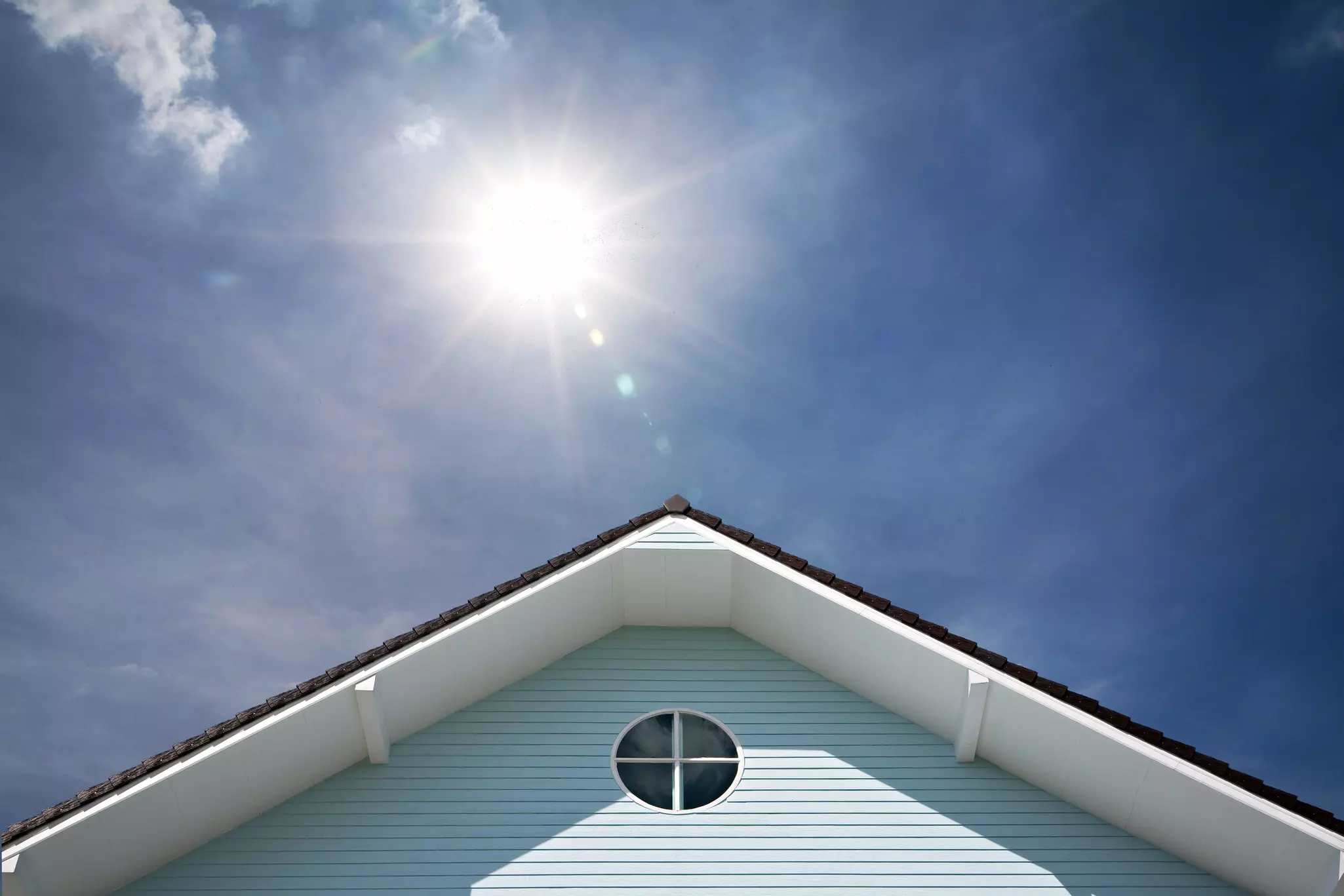 Light blue home gable with vinyl siding under direct sunlight, illustrating heat exposure on a home exterior.