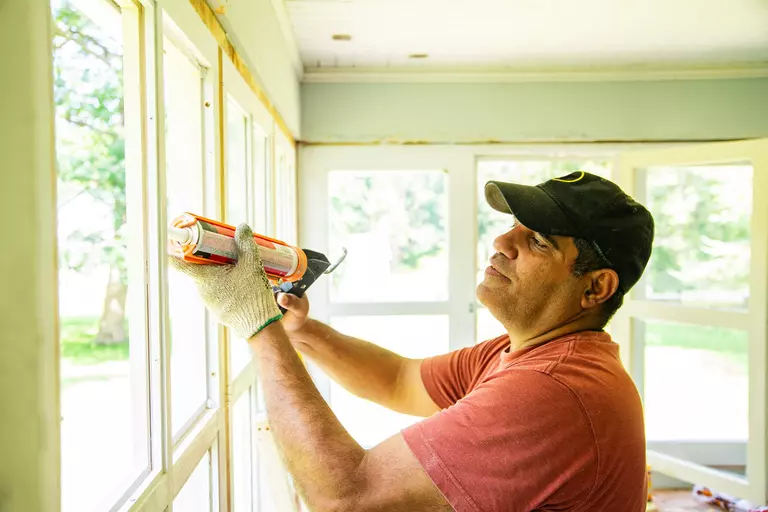 A man reapplying caulk on a window.