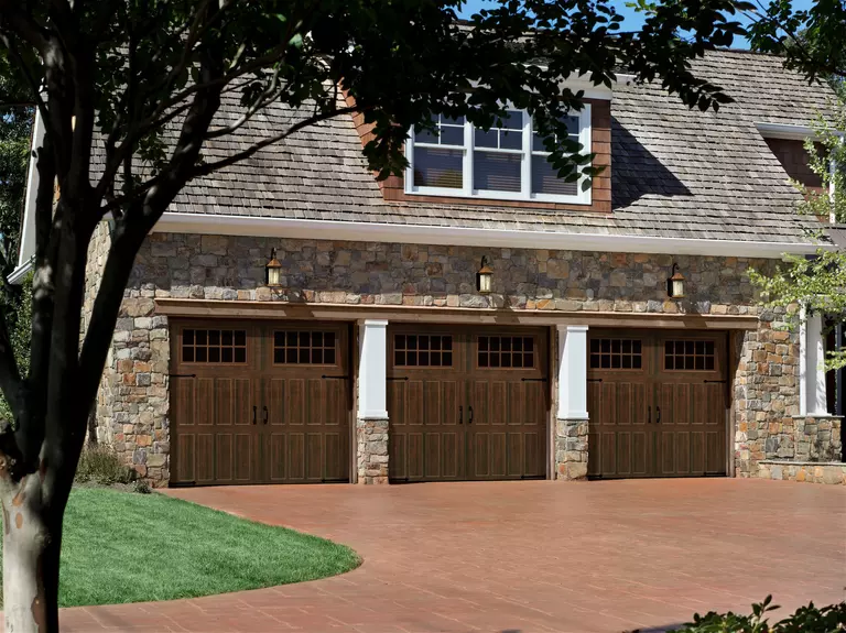 Three similar carriage house-style garage doors on a home with a stone exterior.