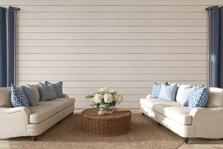 A living room with beige furniture, blue currents and pillows, and a white panel wall in the back.