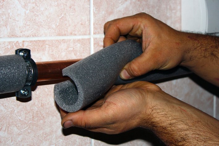 Hands adding pipe sleeves around copper piping as part of home winterization.