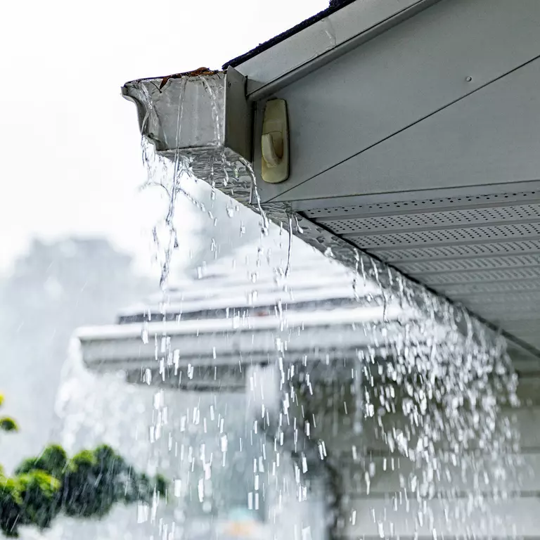 Clogged gutters overflowing with rainwater.