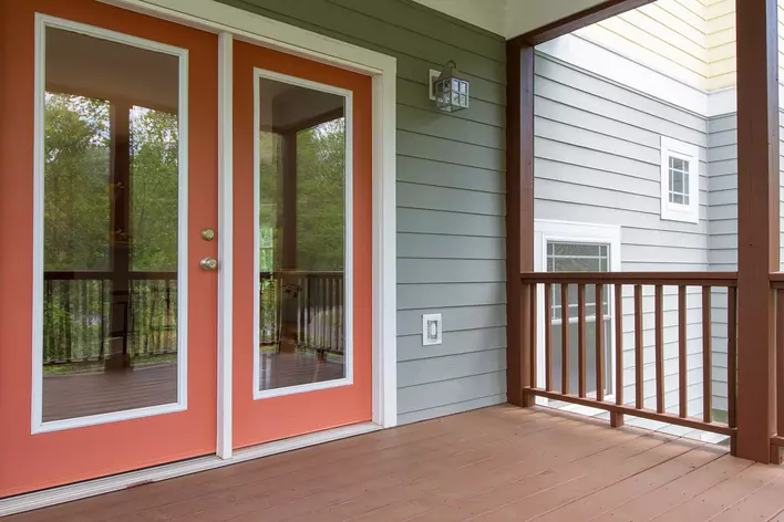 Red and white patio door with a light fixture above it on the side of a gray house
