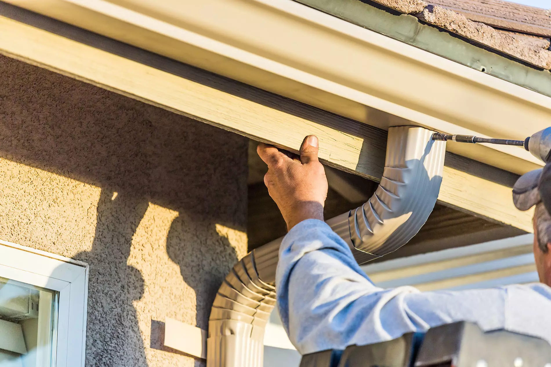 A person installing rain gutters on a house