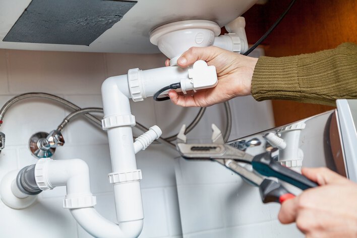 Person checking the plumbing system of their home for leaks as part of summer home maintenance.