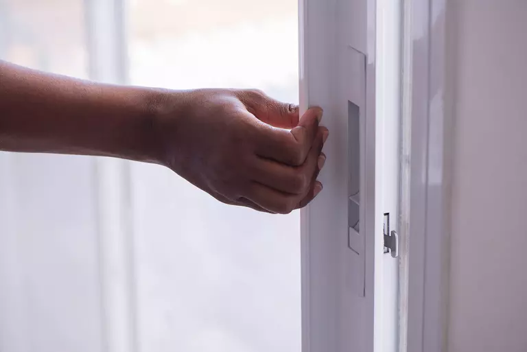 A person grips the handle of a white sliding glass patio door.