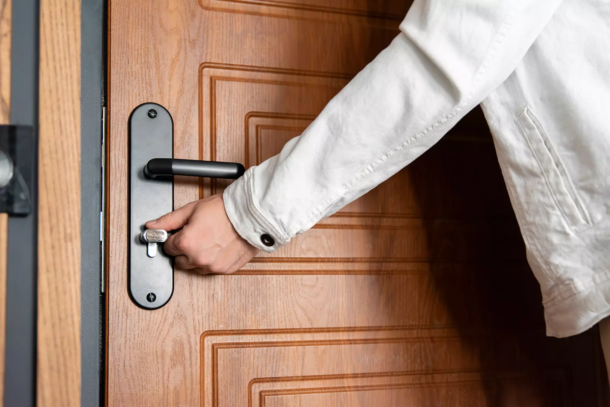 Person turning the lock of a woodgrain entry door.