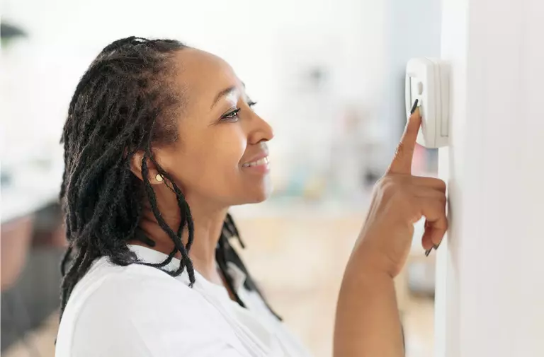 A woman smiling as she programs her thermostat.
