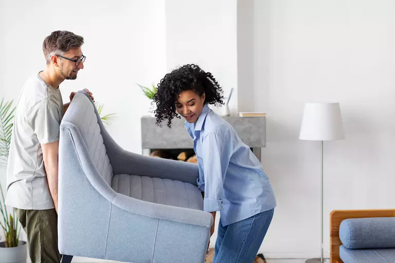 Man and woman lifting a chair together in a living room.