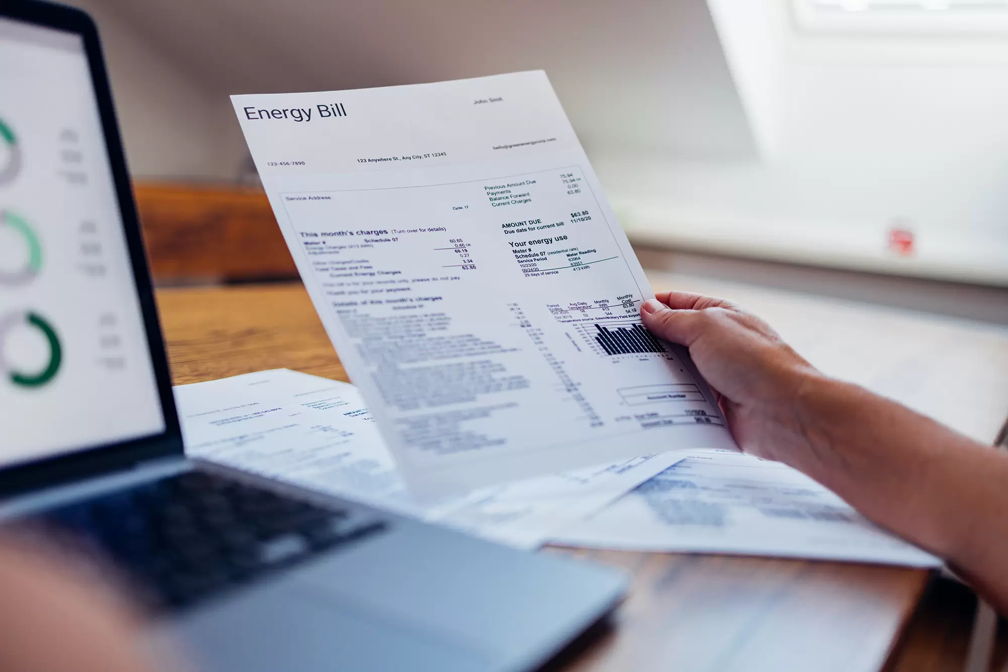 A person reviewing a printed energy bill beside a laptop displaying usage charts.