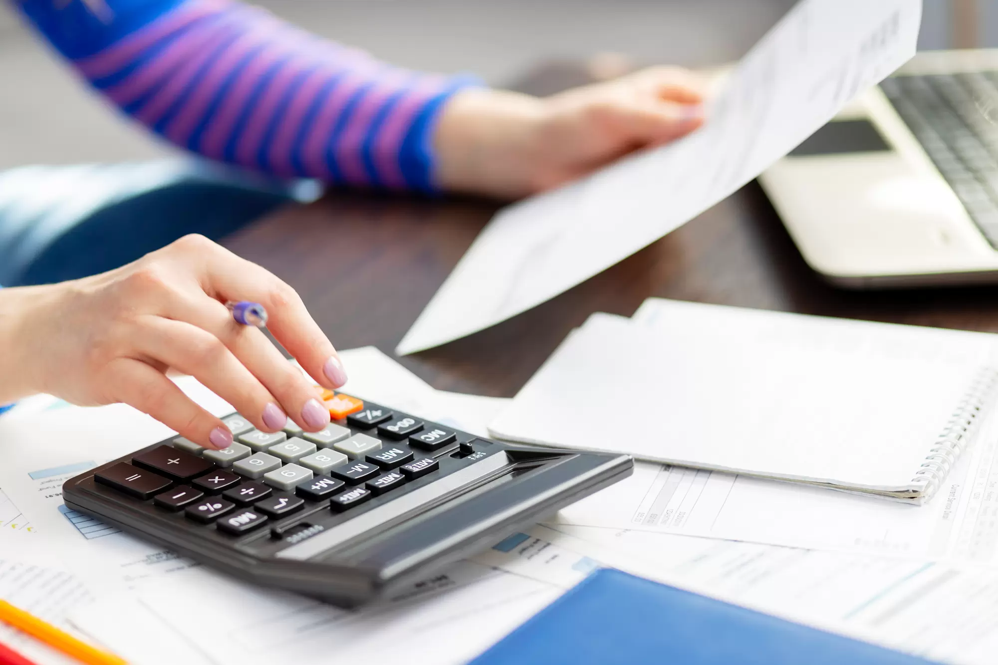 Woman reviewing documents alongside a calculator.