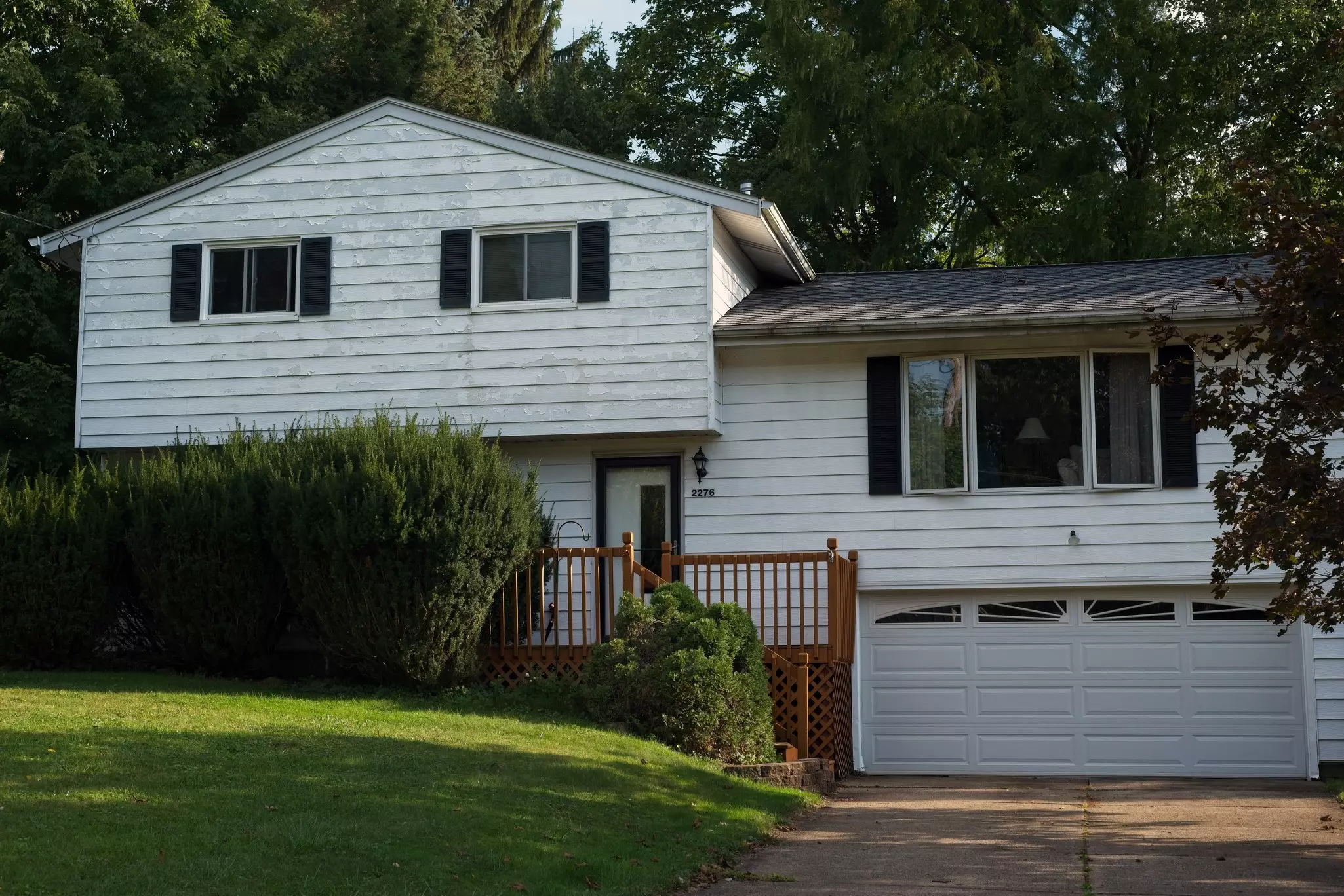 Older suburban home with faded white siding showing UV damage and chalky residue on the surface.