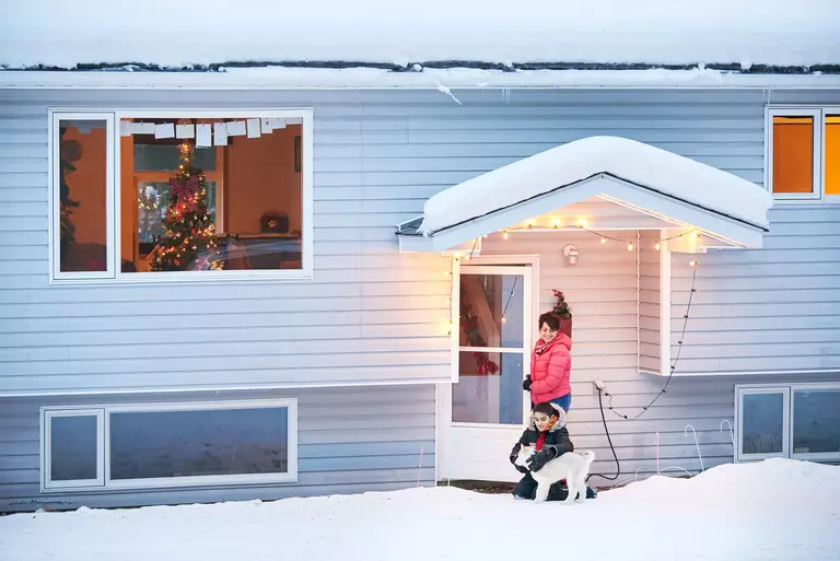 Family and their pet playing in snow just outside of a white storm door.