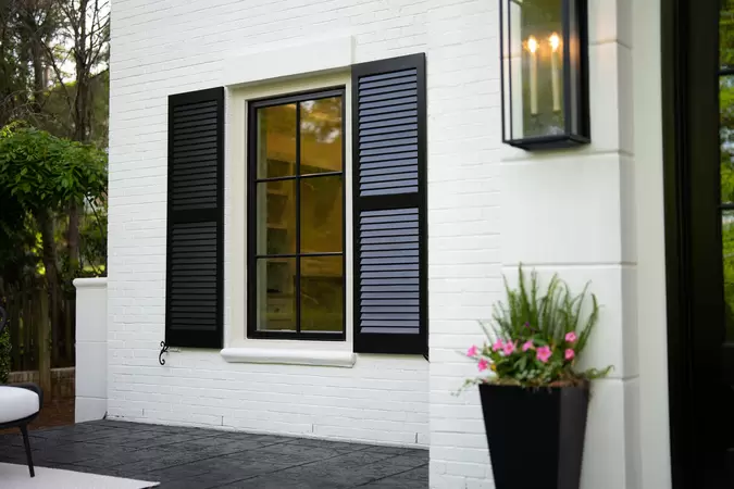 Black wood-clad casement window on a modern white brick home with black shutters