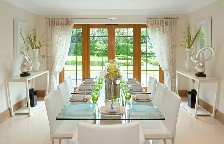 Hinged patio doors decorated with white curtains in a large dining room with neutral tone décor and lots of natural light.