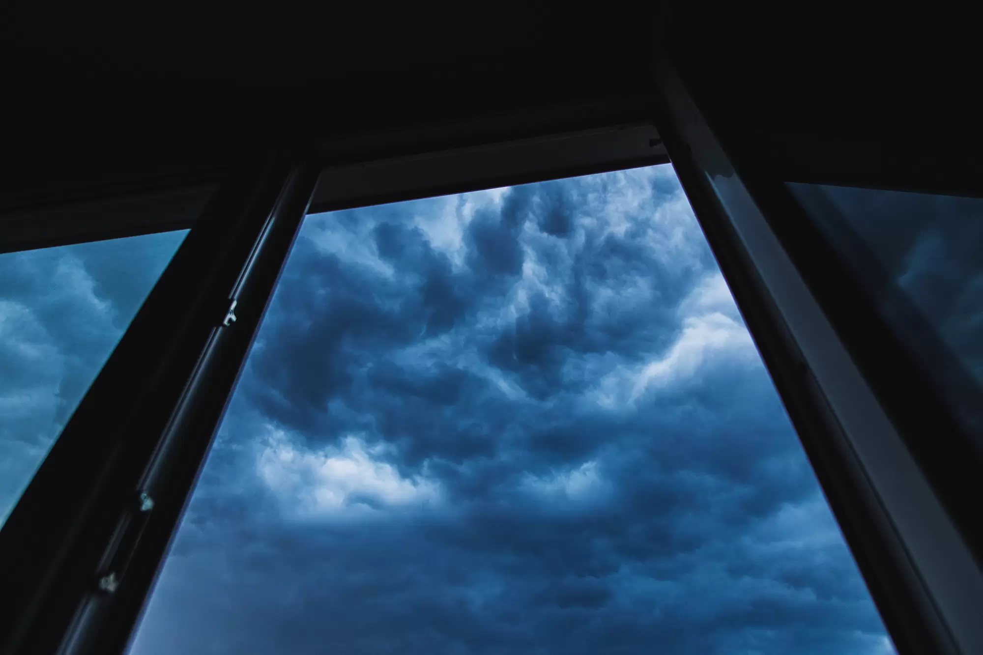 Indoor view of a window looking up at gathering clouds.