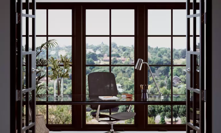 Large casement windows with gridlines behind a desk in a home office.