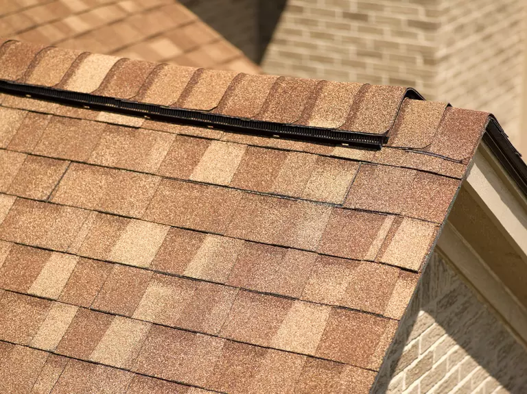 Close-up of tan asphalt roofing shingles with an integrated ridge vent.