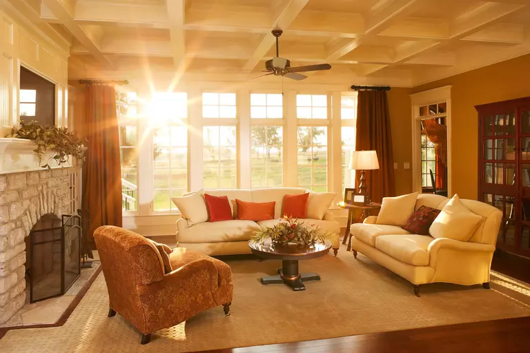 A large living room lit by the evening sun casting a glare through a row of tall windows.