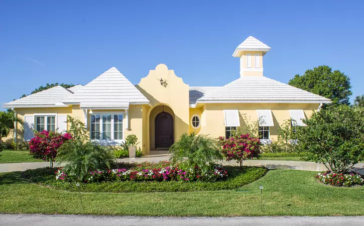 Yard view of yellow house with Bahama shutters on some windows