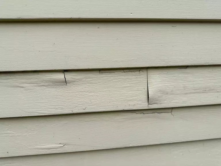 Closeup of cracked and warped white vinyl siding.