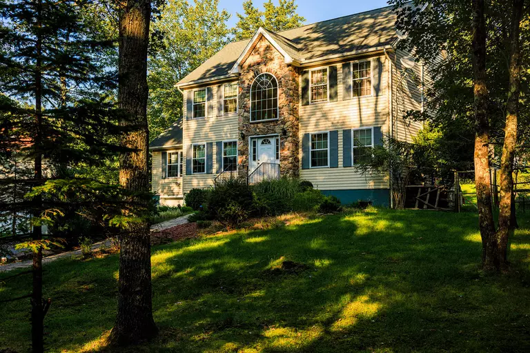 The shaded front lawn of a two-story home with yellow siding, blue shutters, and a stone veneer.
