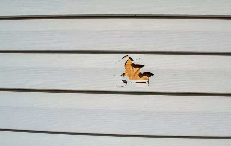 Close-up of damaged vinyl siding with a large hole.