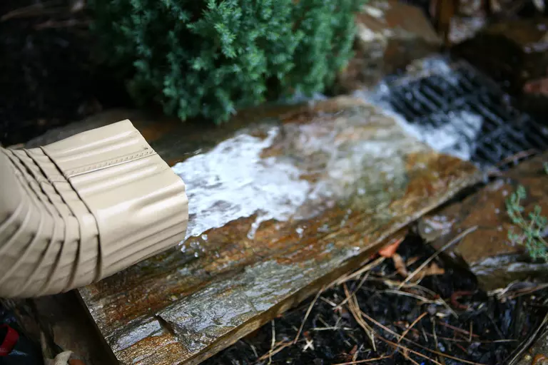 The downspout of a gutter flushing out water onto the ground.